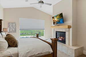 Bedroom featuring vaulted ceiling, a tiled fireplace, ceiling fan, and carpet floors