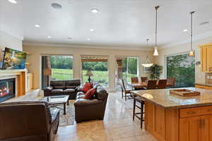 Interior space featuring a tiled fireplace, crown molding, light tile flooring, decorative light fixtures, and a breakfast bar area