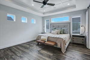 Bedroom featuring dark hardwood / wood-style floors, a barn door, ceiling fan, and a raised ceiling