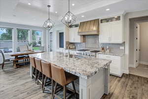 Kitchen with custom range hood, an island with sink, hardwood / wood-style flooring, pendant lighting, and tasteful backsplash