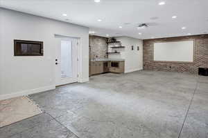 Unfurnished living room with sink, brick wall, and light tile floors