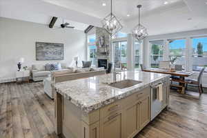 Kitchen featuring a stone fireplace, ceiling fan with notable chandelier, dark hardwood / wood-style flooring, sink, and a kitchen island with sink