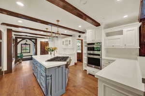 Kitchen featuring hanging light fixtures, stainless steel appliances, hardwood flooring, white cabinets, and beam ceiling