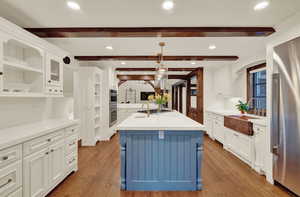 Kitchen with an island with sink, beam ceiling, wood flooring, and pendant lighting