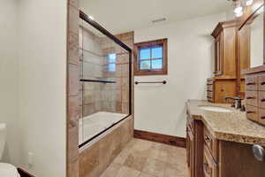 Full bathroom with tile floors, combined bath / shower with glass door, toilet, and vanity