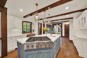 Kitchen with hanging light fixtures, wood flooring, a center island with sink, and white cabinetry