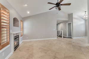 Unfurnished living room featuring a ceiling fan, fireplace, light tile floors, and vaulted ceiling.