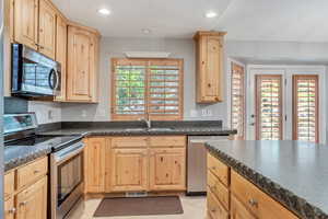 Kitchen featuring a center island, sink, light tile floors, plantation shutters, stone countertops, and stainless steel appliances.