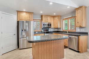 Kitchen with knotty wood cabinetry, stainless steel appliances, a center island, and light tile floors.