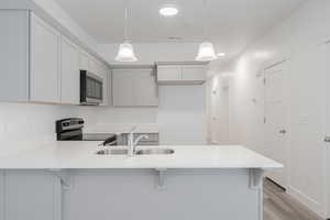 Kitchen featuring appliances with stainless steel finishes, sink, light hardwood / wood-style floors, hanging light fixtures, and a breakfast bar area