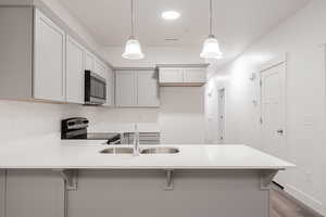 Kitchen with sink, stainless steel appliances, decorative light fixtures, and light wood-type flooring