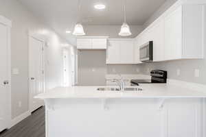 Kitchen with sink, hanging light fixtures, dark hardwood / wood-style floors, range with electric stovetop, and white cabinetry