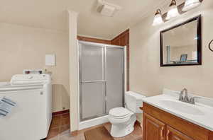 Bathroom featuring washer / dryer, vanity, toilet, tile flooring, and walk in shower