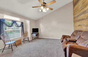 Living area featuring wooden walls, ceiling fan, carpet flooring, and high vaulted ceiling