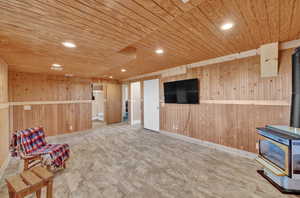 Family room area featuring wooden walls, lvp floor, a wood stove, and wooden ceiling