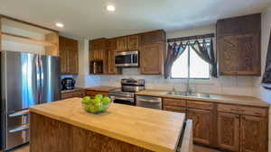 Kitchen featuring butcher block countertops, backsplash, a center island, sink, and appliances with stainless steel finishes