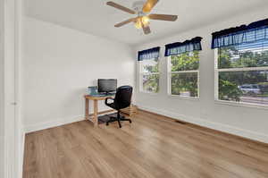 Second bedroom currently used for office space featuring ceiling fan, laminate hardwood flooring, and a wealth of natural light