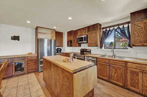 Kitchen with a center island, light tile and laminate flooring, appliances with stainless steel finishes, butcher block countertops, and sink