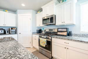 Kitchen with stone counters, appliances with stainless steel finishes, white cabinets, and light tile patterned floors