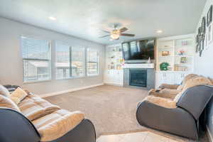 Carpeted living room with a tiled fireplace, built in features, and ceiling fan