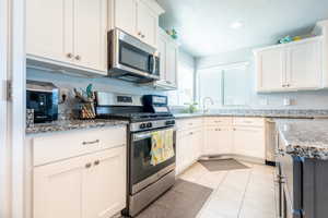 Kitchen featuring light tile patterned flooring, white cabinets, light stone countertops, appliances with stainless steel finishes, and sink