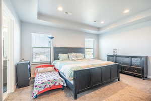 Bedroom with a tray ceiling and light colored carpet