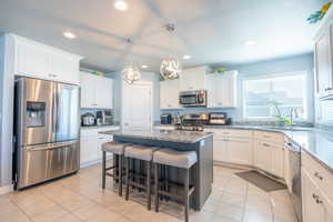 Kitchen with light tile patterned flooring, pendant lighting, light stone countertops, a kitchen island, and appliances with stainless steel finishes