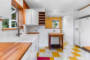 Kitchen featuring white refrigerator with ice dispenser, light tile flooring, track lighting, backsplash, and white cabinetry