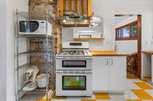 Kitchen featuring white appliances, butcher block countertops, light tile flooring, backsplash, and white cabinetry