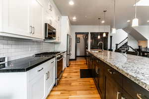 Kitchen with light wood-type flooring, appliances with stainless steel finishes, white cabinets, pendant lighting, and sink