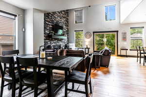 Dining area featuring a stone fireplace, a towering ceiling, plenty of natural light, and light wood-type flooring