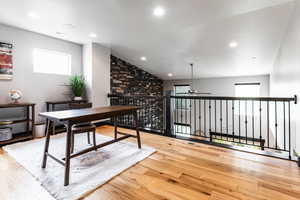 Home office featuring ceiling fan, light hardwood / wood-style floors, lofted ceiling, and brick wall