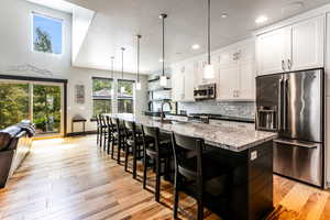 Kitchen featuring hanging light fixtures, tasteful backsplash, a kitchen island with sink, light wood-type flooring, and appliances with stainless steel finishes