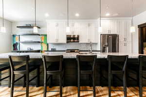 Kitchen featuring stainless steel appliances, a center island with sink, light hardwood / wood-style flooring, and decorative light fixtures