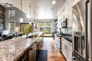 Kitchen featuring tasteful backsplash, decorative light fixtures, light wood-type flooring, high end appliances, and sink