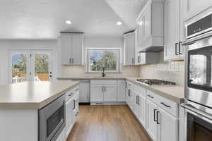 Kitchen featuring a textured ceiling, stainless steel appliances, sink, white cabinets, and light hardwood / wood-style floors