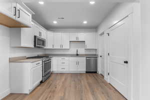 Kitchen with light wood-type flooring, white cabinetry, stainless steel appliances, and sink