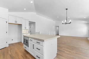 Kitchen with a kitchen island, stainless steel microwave, white cabinetry, and light hardwood / wood-style floors