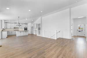 Unfurnished living room featuring a textured ceiling, an inviting chandelier, light hardwood / wood-style flooring, sink, and high vaulted ceiling