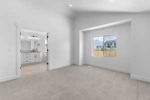 Unfurnished bedroom featuring lofted ceiling, light colored carpet, ensuite bathroom, and sink