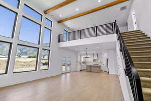 Unfurnished living room with beamed ceiling, a towering ceiling, a chandelier, and light hardwood / wood-style floors