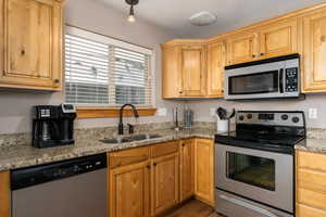 Kitchen featuring light stone counters, appliances with stainless steel finishes, sink, and hardwood / wood-style floors
