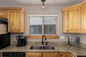 Kitchen featuring dishwasher, sink, light stone counters, and pendant lighting