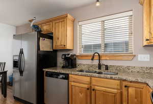 Kitchen with light stone counters, sink, wood-type flooring, and appliances with stainless steel finishes