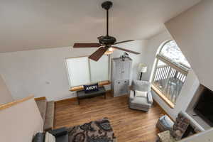 Living room featuring hardwood / wood-style flooring, ceiling fan, a fireplace, and lofted ceiling