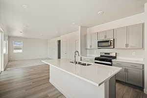 Kitchen featuring sink, a center island with sink, light hardwood / wood-style floors, appliances with stainless steel finishes, and gray cabinetry