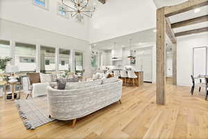 Living room with light hardwood / wood-style floors, beam ceiling, a high ceiling, a chandelier, and sink