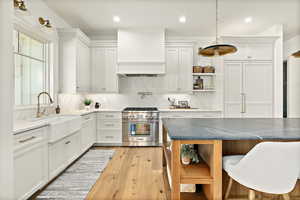 Kitchen with high end stainless steel range, custom range hood, light hardwood / wood-style flooring, decorative light fixtures, and backsplash