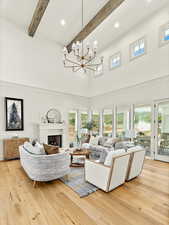 Living room featuring beam ceiling, light hardwood / wood-style floors, a towering ceiling, and a chandelier