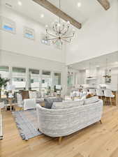 Living room featuring a notable chandelier, beamed ceiling, a high ceiling, and light hardwood / wood-style flooring